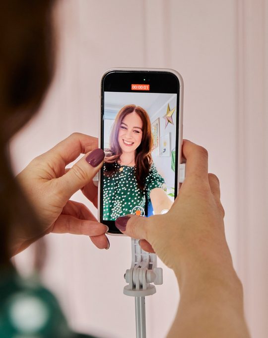 Smiling business owner filming a quick offer video on a phone held on a tripod